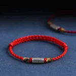 Red woven lucky bracelet with sterling silver everything goes well charm on dark blue background