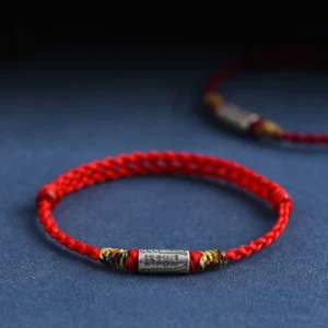 Red woven lucky bracelet with sterling silver everything goes well charm on dark blue background