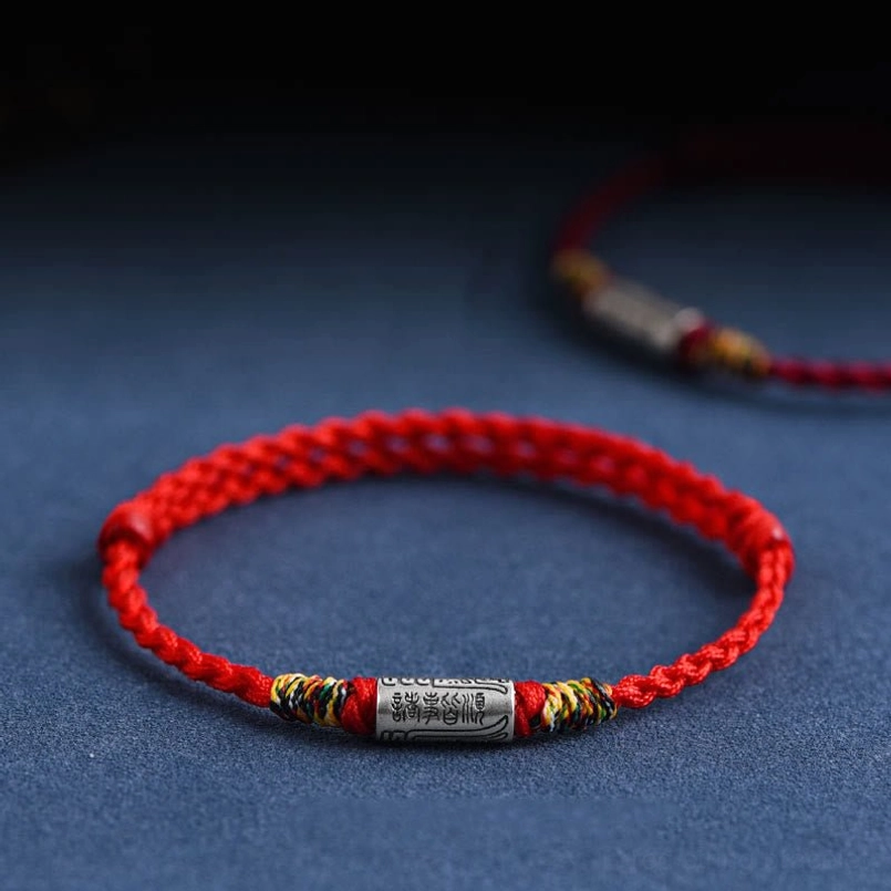 Red woven lucky bracelet with sterling silver everything goes well charm on dark blue background