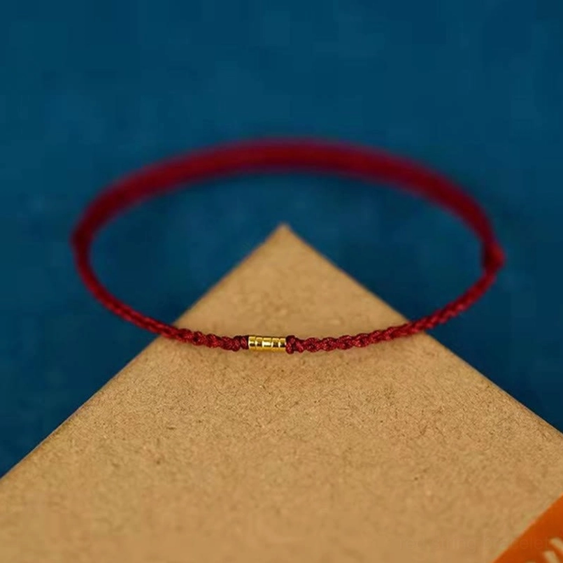 Fine woven red string bracelet with golden center bead on brown paper