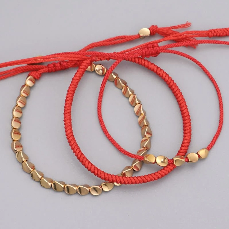 Multiple red string fortune bracelets arranged flat lay with copper beads scattered display