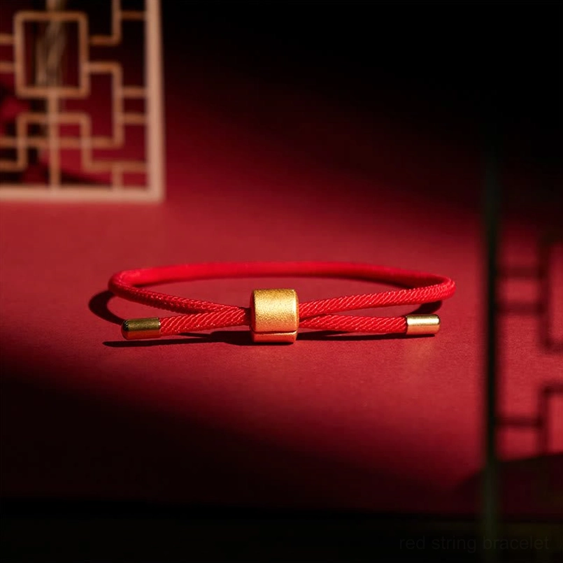 Red string bracelet flat lay display matte gold clasp dark red background