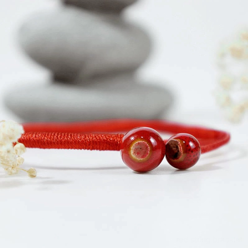 Flat lay side view of feng shui red string bracelet with stacked stone and floral decor