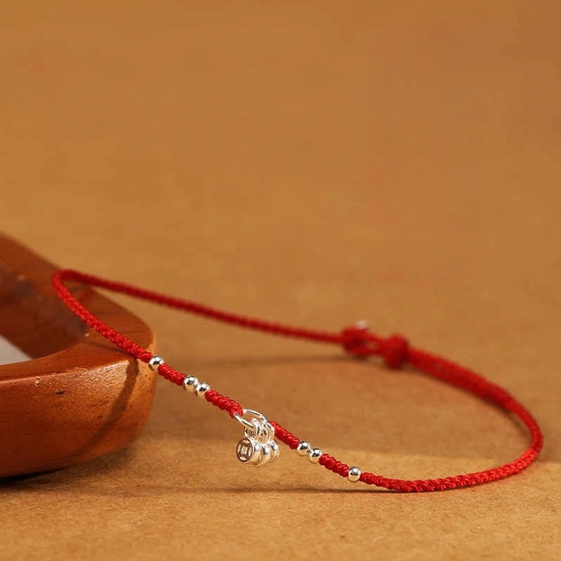 Handcrafted red string bracelet flat lay display with wooden background and single silver coin charm