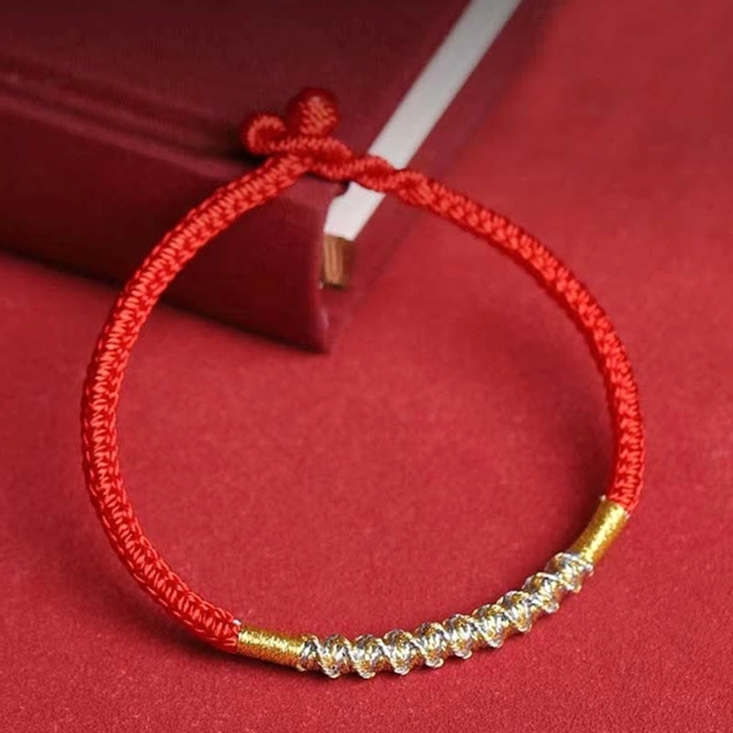 Red string protection bracelet flat lay front view with spiral gold bead decoration on book