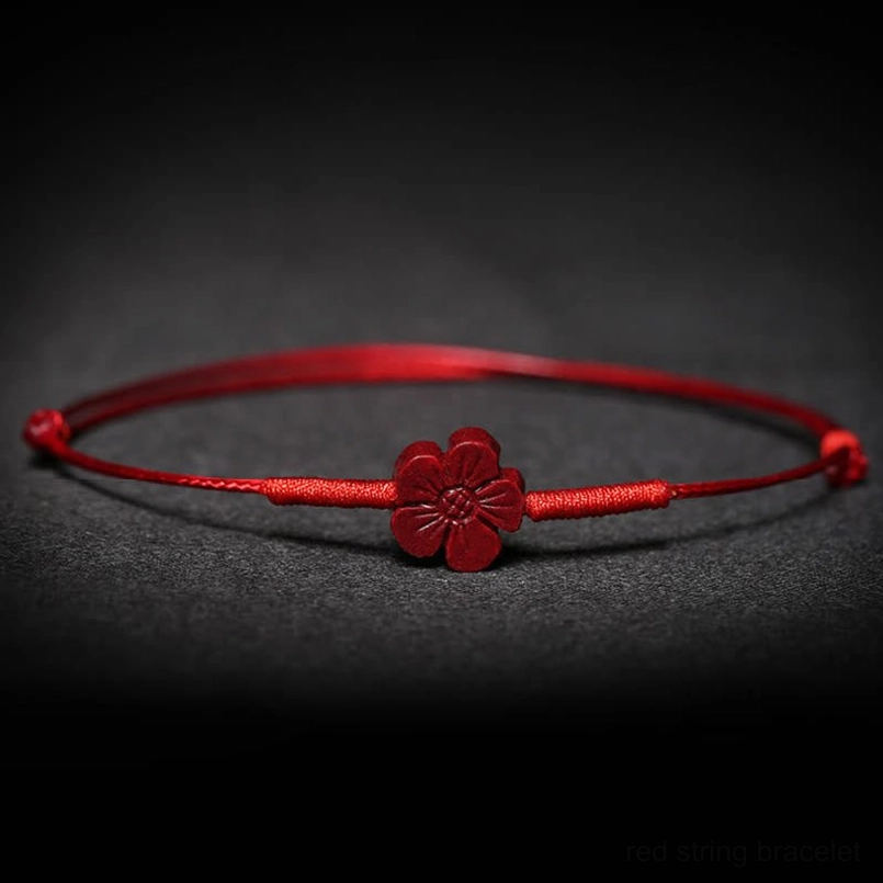 Red cord bracelet with four-leaf clover charm flat lay