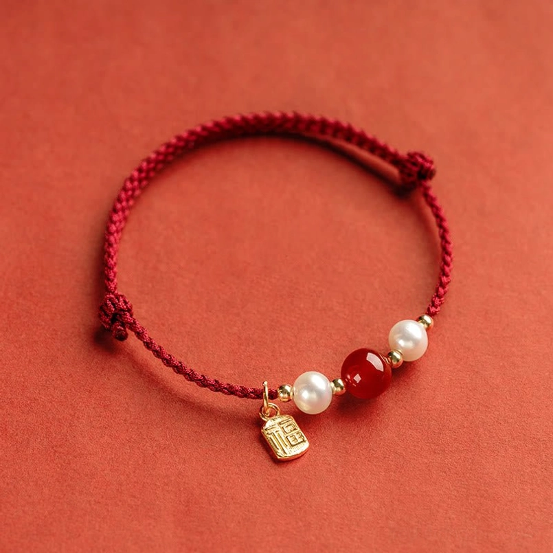 Red string fortune bracelet with small gold Fu charm and pearl bead arrangement angled side view
