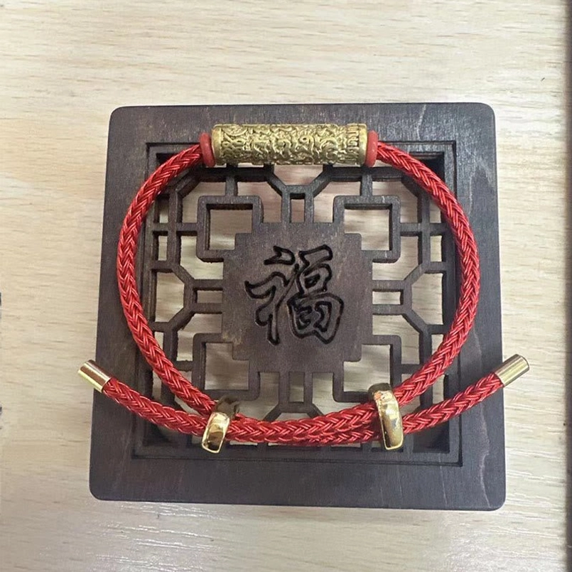Red Tibetan string bracelet with gold metal embossed charm on traditional feng shui wooden plaque