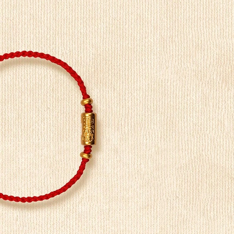 Red braided rope bracelet with 999 gold barrel charm - flat lay top view
