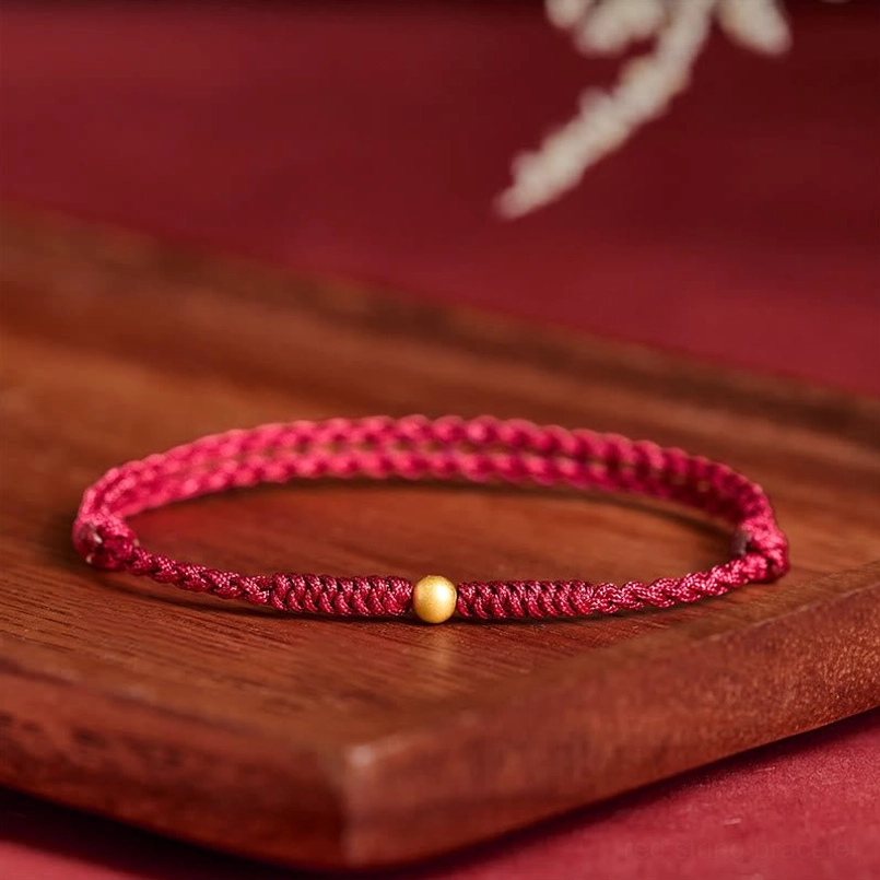 Red string protection bracelet with central gold bead on wooden display