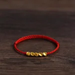 Red string braided protection bracelet with gold beads oblique view