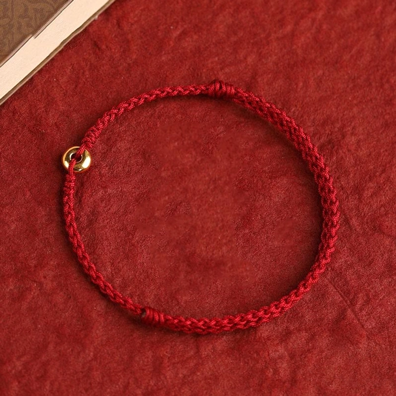 full view 999 gold peace buckle red string bracelet flat lay on red fabric