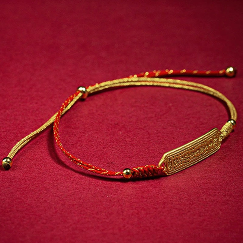 Red string bracelet with engraved gold plaque flat lay on dark red fabric