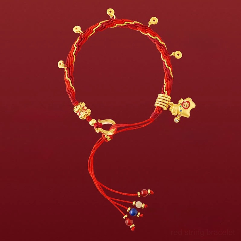 Red string luck bracelet flat lay featuring gold toggle clasp, decorative pendants, and beaded tassel on red backdrop