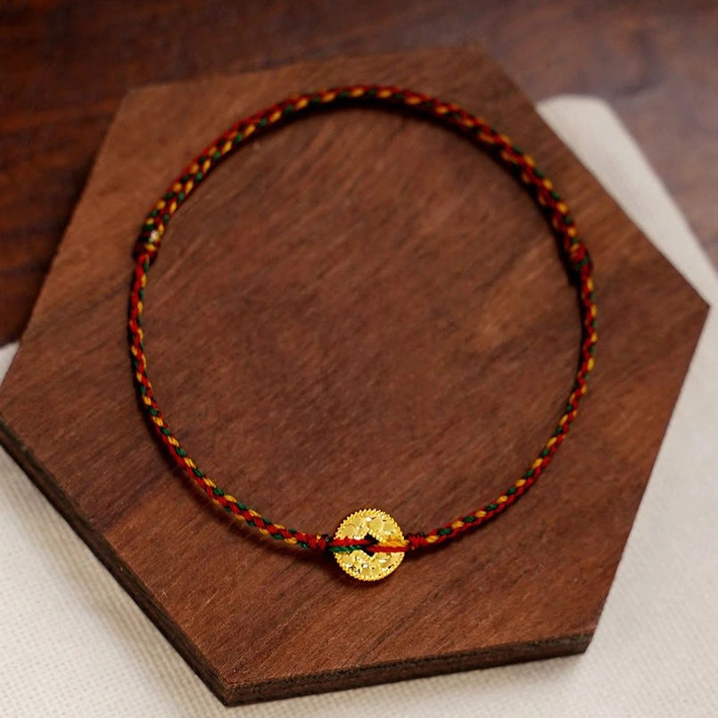 Woven mixed-tone red string bracelet with central gold coin pendant on hexagonal wooden board