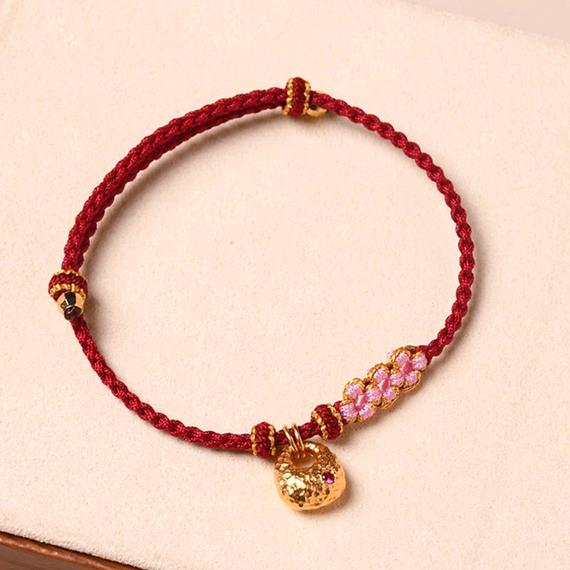 Red rope protection bracelet with gold pendant and peach blossom charm detail