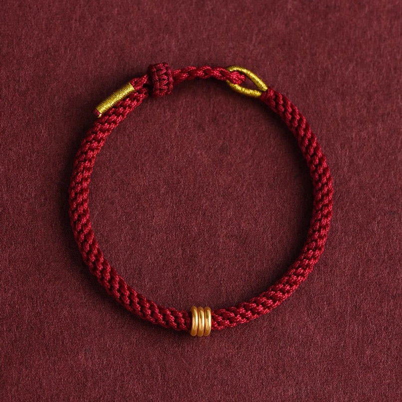 Handmade red braided rope bracelet with gold triple ring accent flat lay design