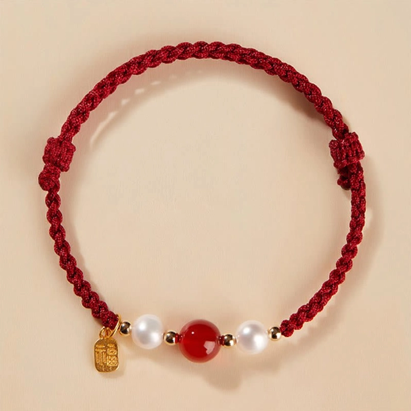 Single red string fortune bracelet with gold tag pendant and red agate pearl details on light beige background
