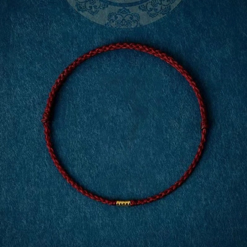 Single braided red string bracelet with golden center bead on dark blue fabric