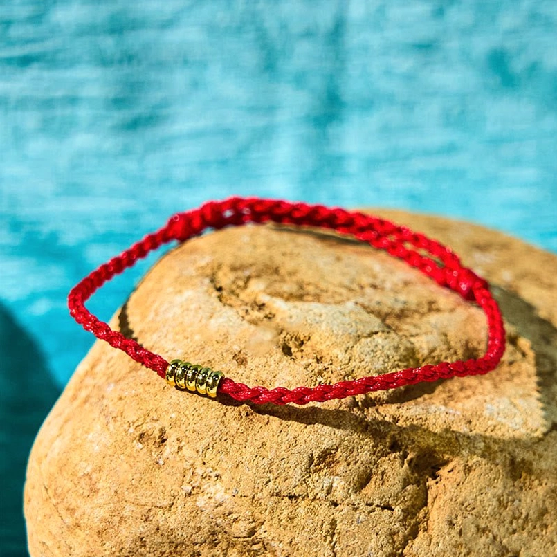 Red string bracelet with golden beads overhead flat lay shot