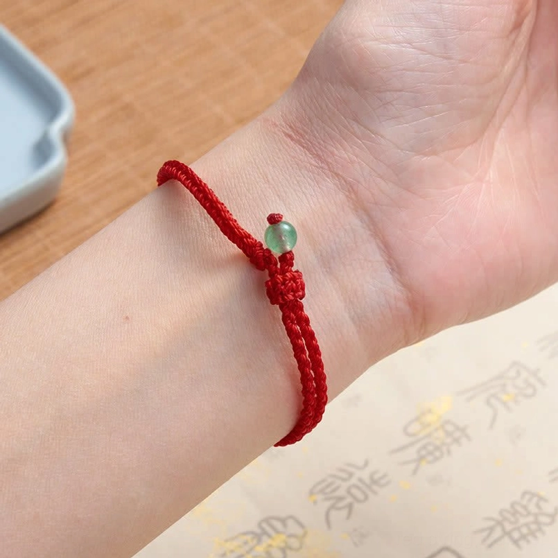 Red string balance bracelet worn on wrist with green aventurine bead side close-up view