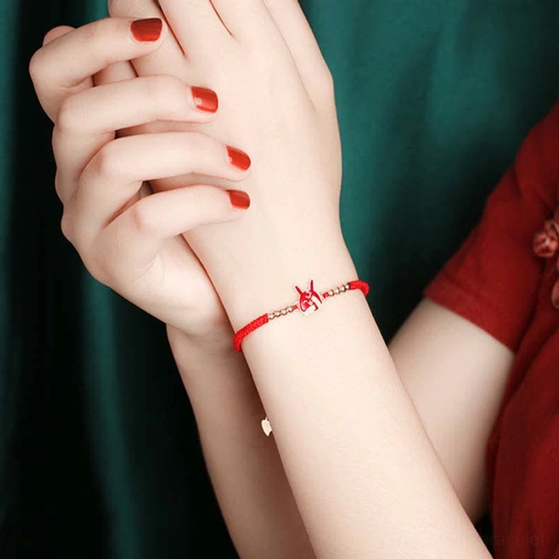Delicate red string bracelet held in hand with cheongsam background showing bracelet size
