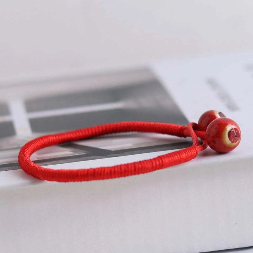 Three-quarter view of red woven cord bracelet with adjustable ceramic bead stopper