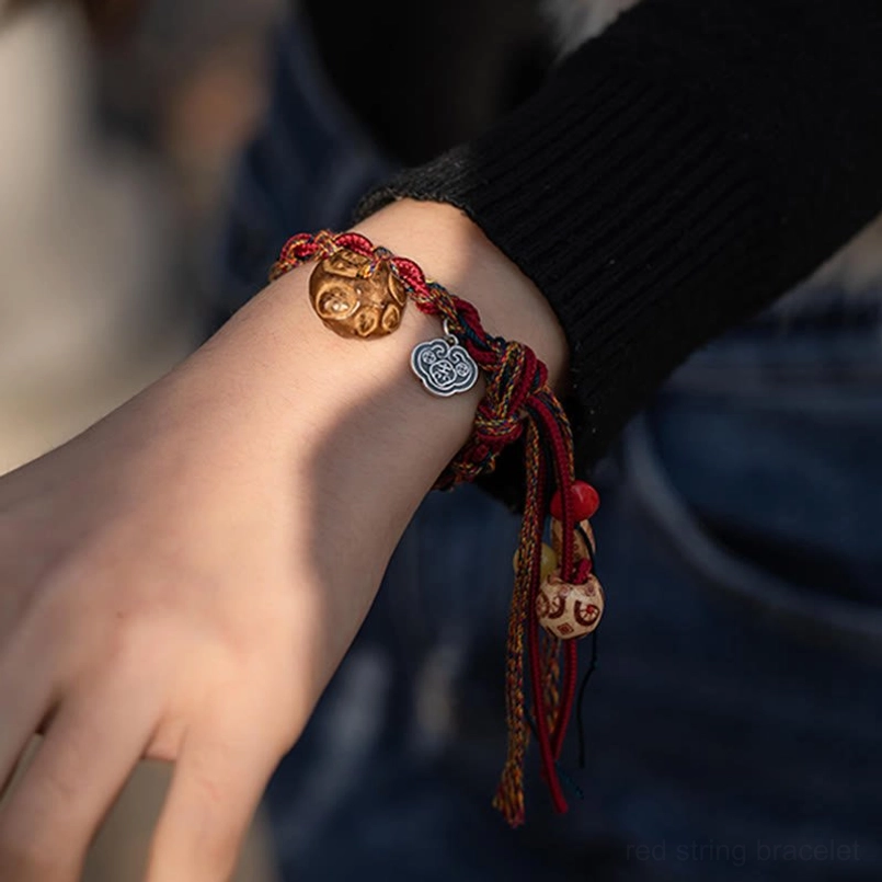 Tibetan red string bracelet on wrist showing carved koi fish metal charm and silver cloud design