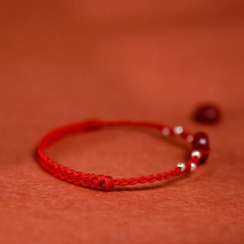 Minimalist red braided string bracelet with silver beads and red closure on textile background