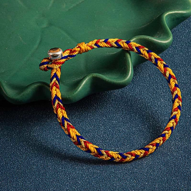 Multicolor red string bracelet displayed with green decorative leaf prop emphasizing natural and spiritual elements