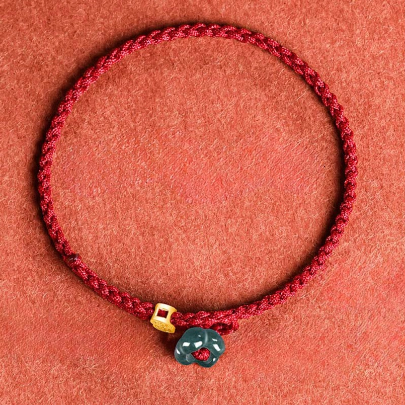 Red braided bracelet overhead view with gold bead and jade charm detail