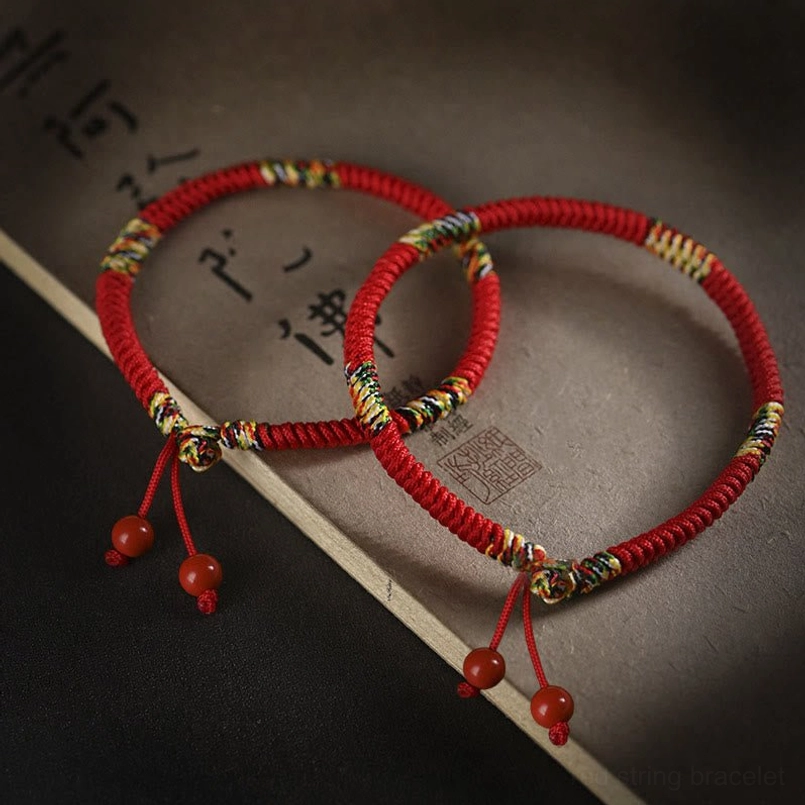 Pair of five-color red string bracelets with five dhyani buddhas design and cinnabar charms flat lay