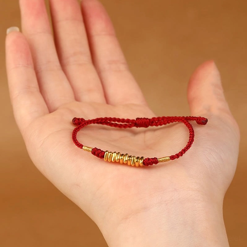 999 gold red string luck bracelet resting on palm