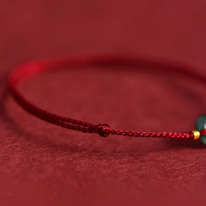 Red string bracelet partial view with thin woven cord and jade peace buckle charm on red background