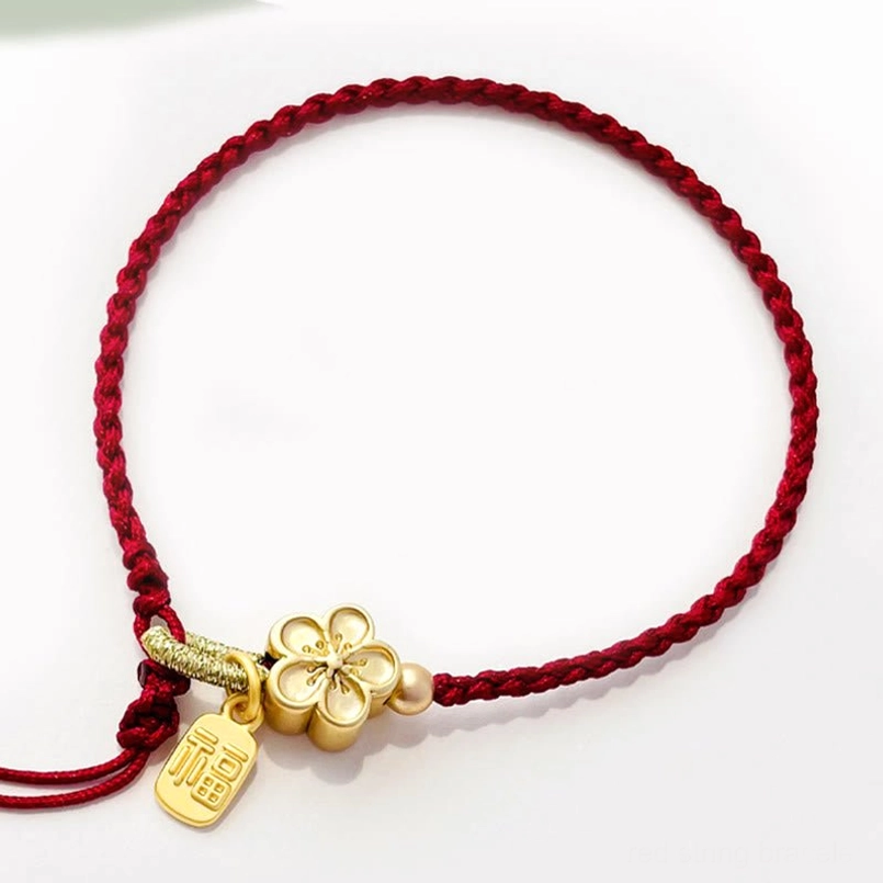 Side view of red braided string bracelet with gold four-leaf peach blossom charm and Fu character pendant