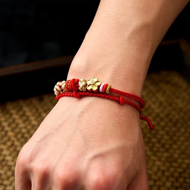 Red peach blossom bracelet worn on wrist showing adjustable rope tails