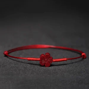 Red string blessing bracelet with plum blossom charm flat lay