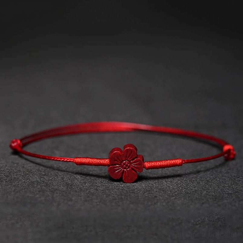 Red string blessing bracelet with plum blossom charm flat lay