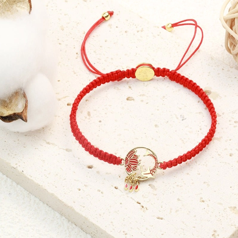 Adjustable red lucky string bracelet with lotus koi fish pendant displayed on cotton - overhead angle