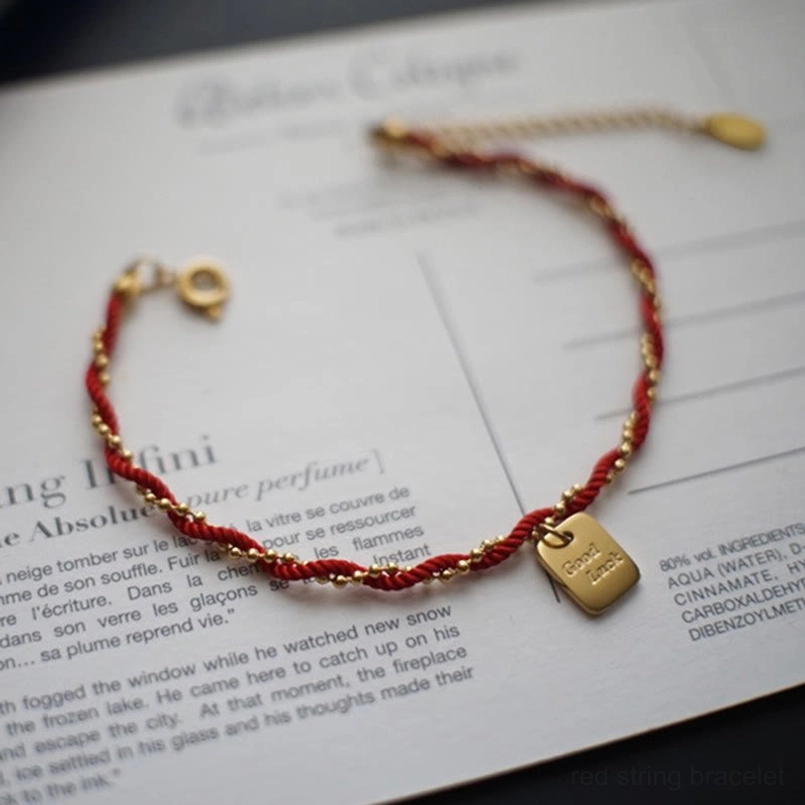 Red rope gold charm bracelet oblique overhead view with round metal clasp detail
