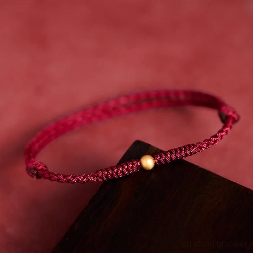 Braided red string bracelet with single gold bead, three-quarter view