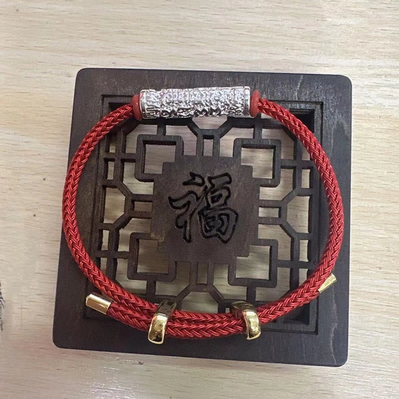 Red woven Tibetan protection bracelet with silver metal tube ornament on blessed wooden background