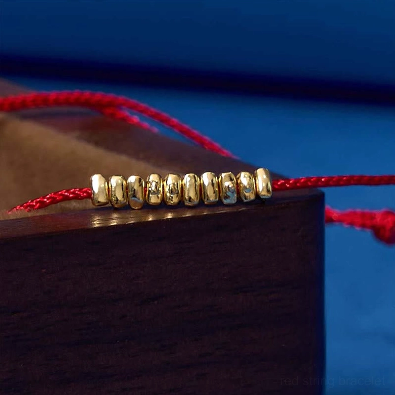 Detailed extreme close-up of small silver beads on red string bracelet