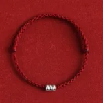 Red braided lucky bracelet with sterling silver beads on red fabric background, flat lay view