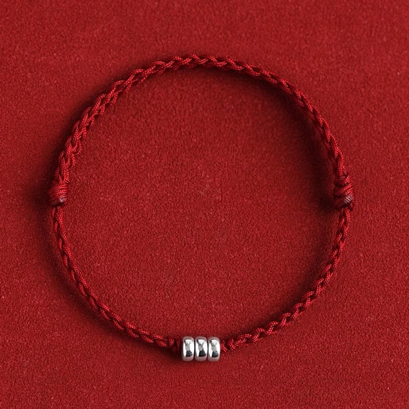 Red braided lucky bracelet with sterling silver beads on red fabric background, flat lay view