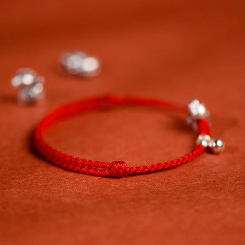 Red cord bracelet with silver charms and adjustable knot closure overhead view