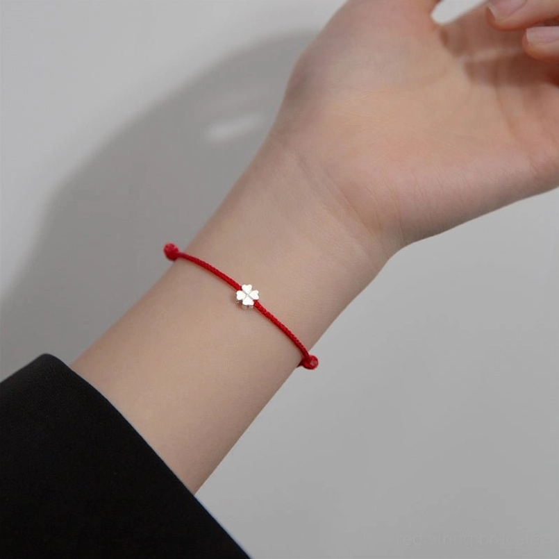 adjustable red cord bracelet with tiny silver clover charm on slender wrist