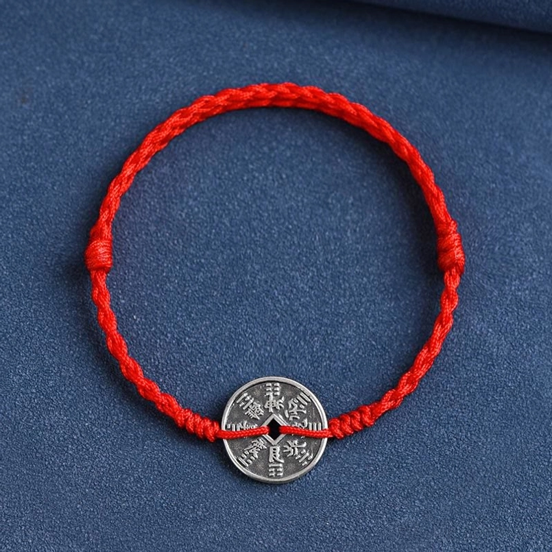 Red woven bracelet with 925 sterling silver coin centered on dark background