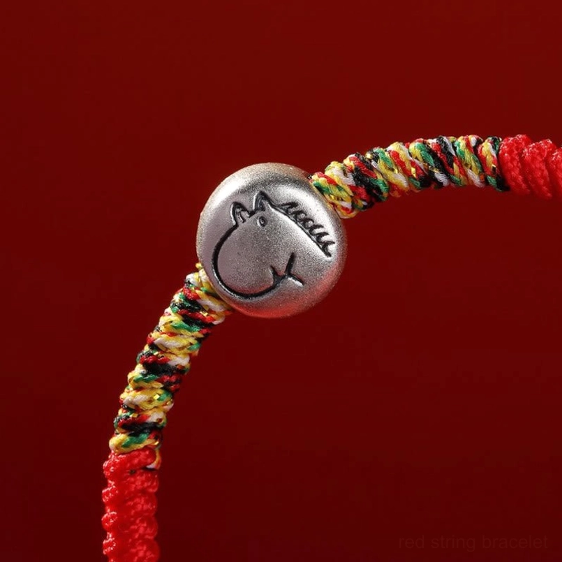 Close up detail of silver horse charm and red braided string joint