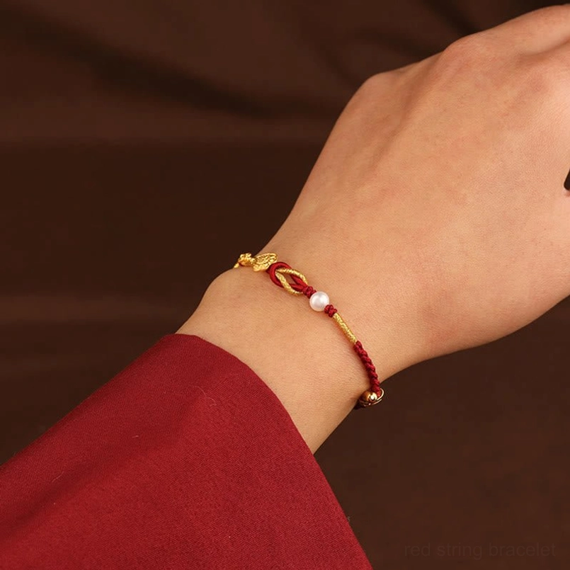 Adjustable red string bracelet with sliding metal adjuster and gold charms on wrist close-up